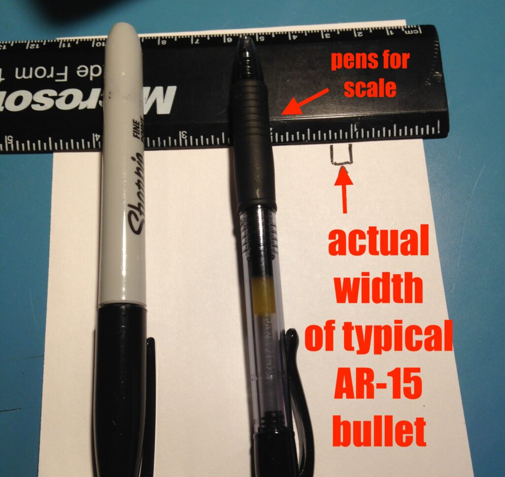 A ruler and two pens on a piece of paper, with the width of a typical AR-15 projectile / bullet indicated on the ruler. It is much narrower than either pen.