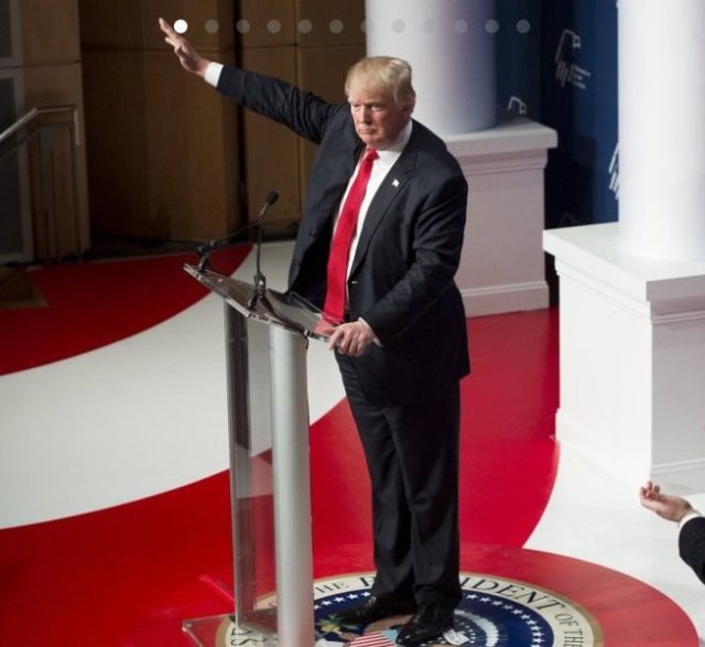 Trump, in 2016, standing in front of a podium on top of a red carpet with the Presidential Seal of the United States giving what looks like a Nazi salute.