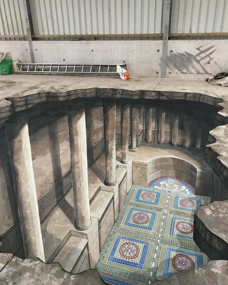 A stunning 3D street art illusion by Joe and Max depicting the interior of an ancient temple with grand marble columns and intricately tiled floors. The artwork creates the illusion of a massive hole in the concrete floor, revealing a hidden underground structure. Natural light and realistic shadows enhance the depth and architectural details, making it appear as though the viewer could step into this subterranean world.