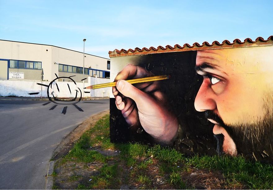 A playful 3D mural by Cosimo Cheone Caiffa, depicting a hyper-realistic man holding a pencil and appearing to draw a sun on a nearby wall. The artwork cleverly integrates the surrounding environment, using the road as part of the composition to create the illusion of the sun's rays extending beyond the mural. The man's focused expression and detailed features, combined with the whimsical interaction between the painted and real-world elements, make this piece a stunning example of Cheone's imaginative and interactive street art.