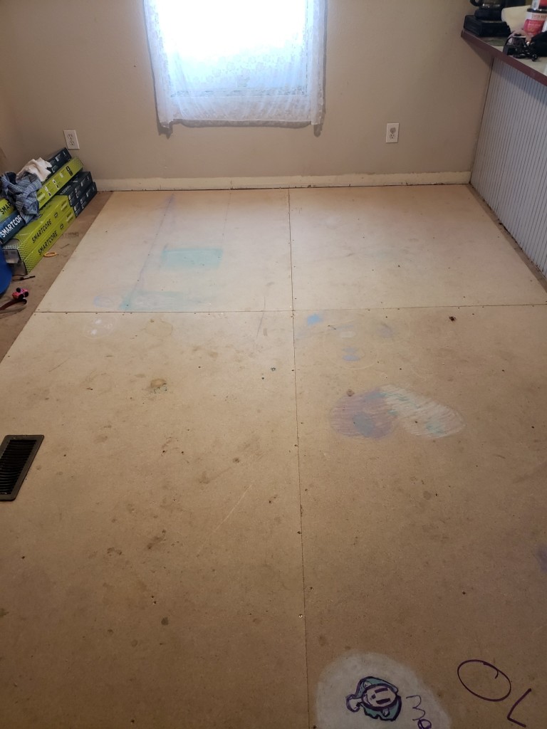 Two full, and two partial sheets of particle board subfloor installed in a dining room. Off on the left can be seen a few boxes of wood laminate flooring

The subfloor is decorated with chalk