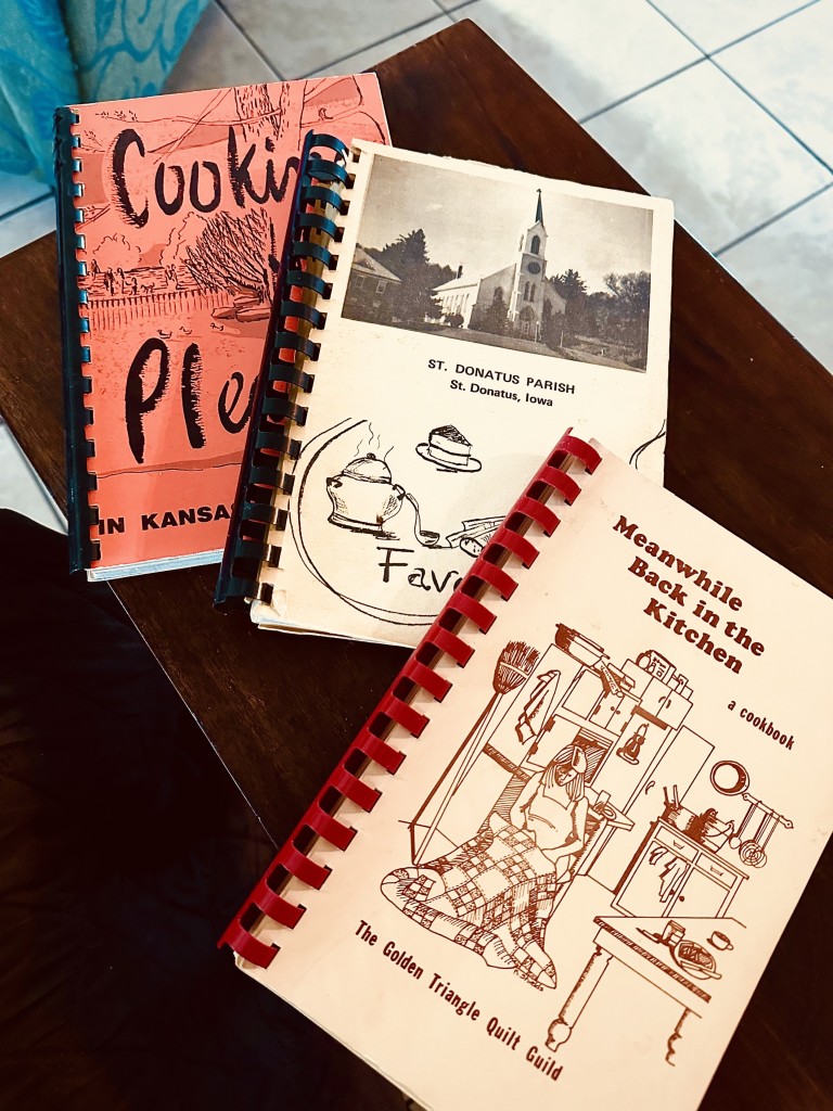 3 fundraiser cookbooks decades old: Kansas City, St Donatus Iowa, and Beaumont Texas. All have classic plastic binder spines and the covers look very Old Skool drawings and lettering. 