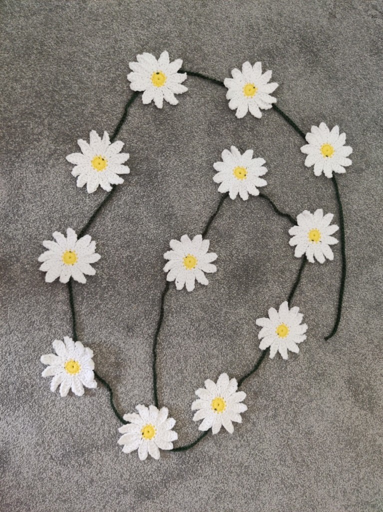 Crocheted daisies connect by a green crocheted chain