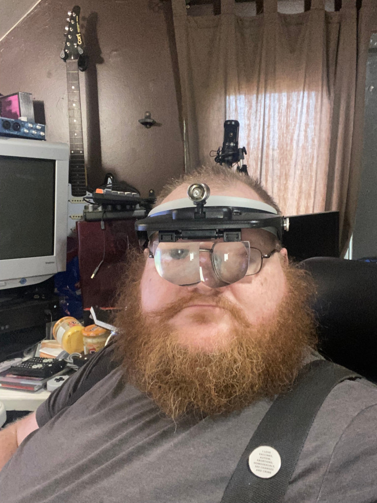 A red-bearded man in his early 40s sits in an office wearing a head-mounted magnifier