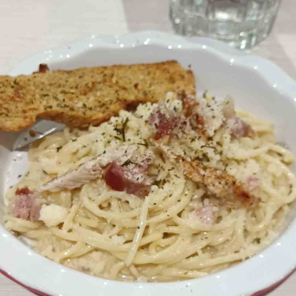 Photo of a pasta carbonara with garlic bread on the side