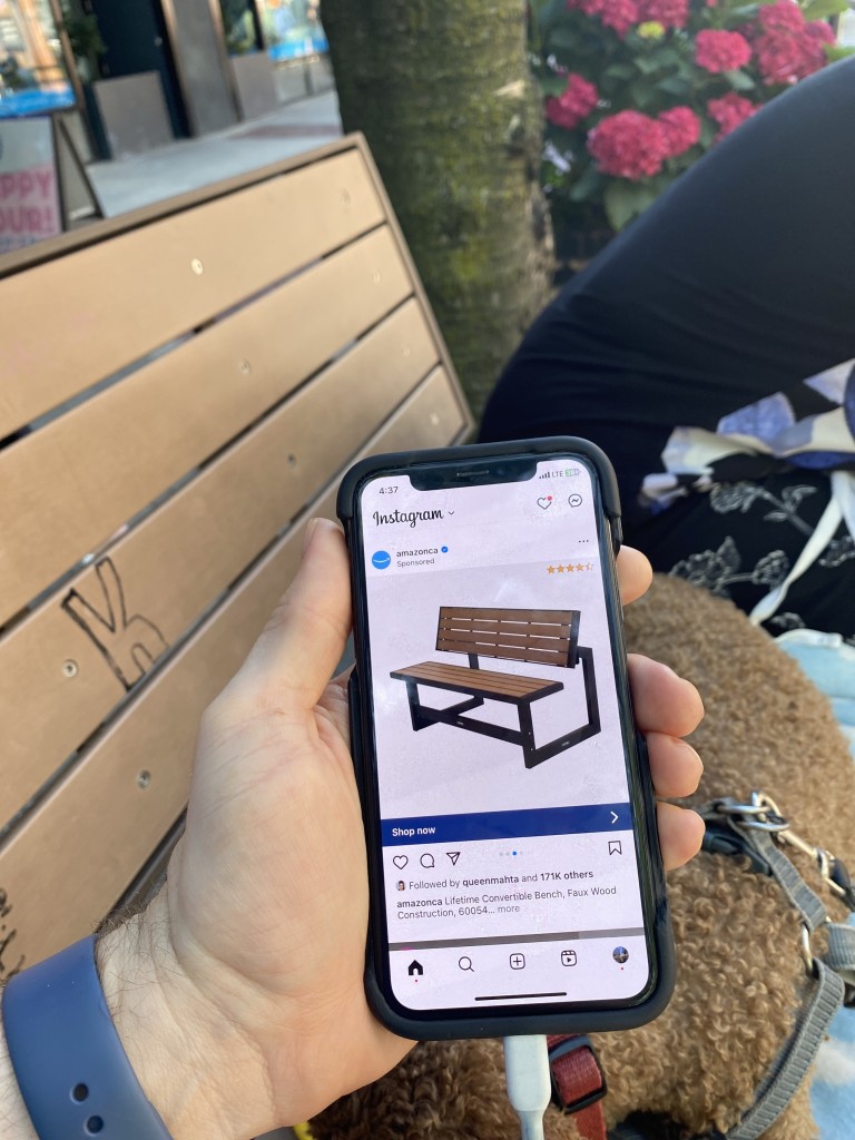 A phone displaying an Amazon ad for the same specific bench, with the bench visible in the background