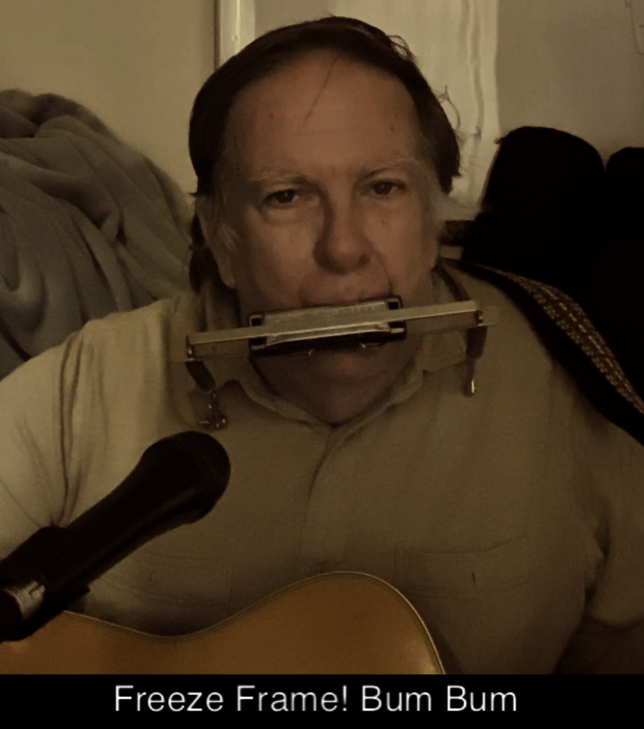 Yours truly, Dan of The Pomegranate County Irregulars, holding a pose with guitar and harmonica in brace at the end of a solo acoustic video of the song “John Hardy, the Boss, and the Judge.”I did exclaim “Freeze frame! Bum bum”, a reference to a J. Geils Band hit from the 1980s, and duly added it to the caption.