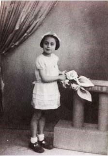 Vintage black and white photo of a child dressed in a formal outfit with a hat and holding flowers