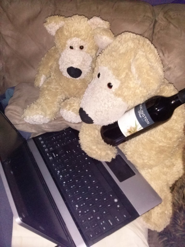 Two teddy bears one slightly larger. His name is mookie. He's tan with a long snoze and a black nose and his brother doofus looks identical to him but smaller mookie is holding a bottle of wine while both of them staring at a laptop screen