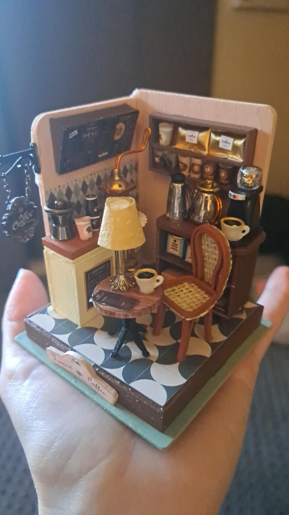 a very small cofe shop in my tiny hand. there's a chair, table, a counter, a menu, lots of little accessories. some glue and rough edges are visable 