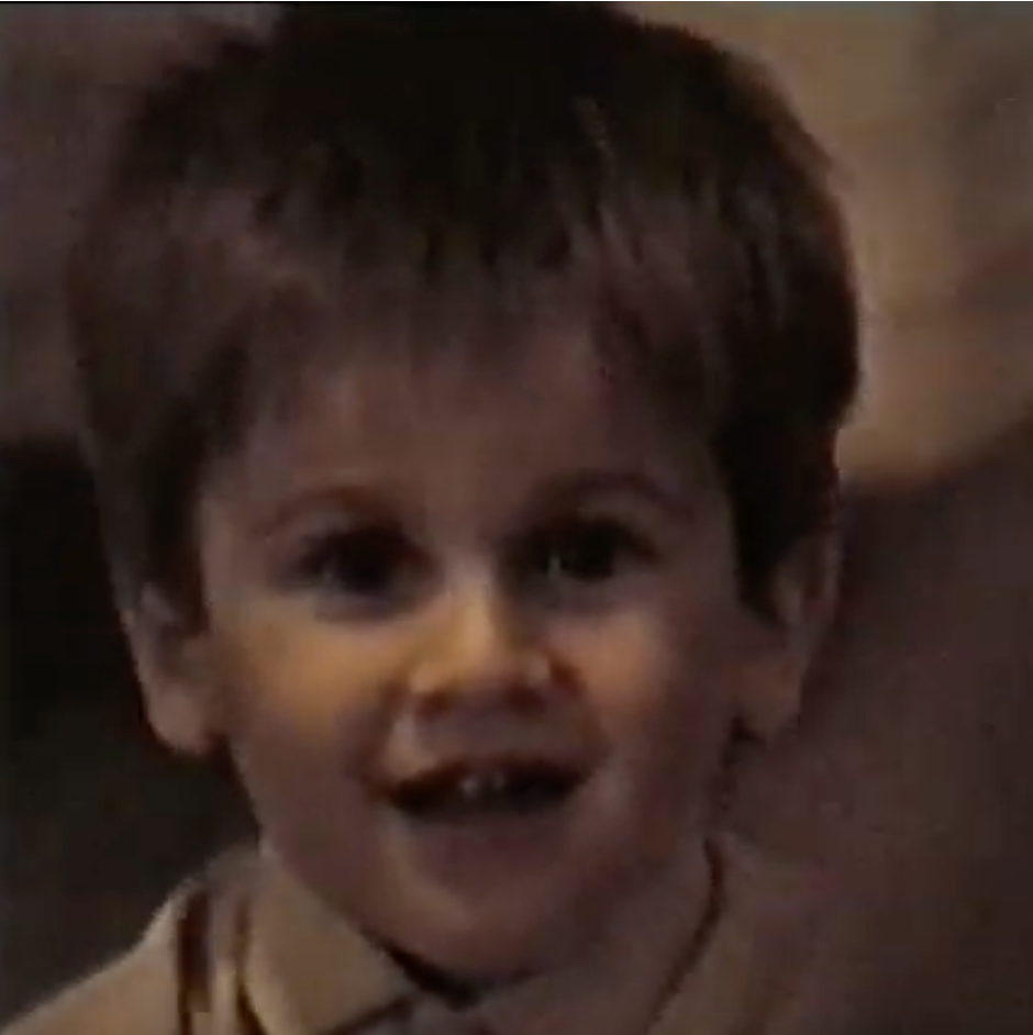 A childhood photo from 1983 showing a young child smiling with joy. The child has short blonde/brown hair and is wearing a beige shirt, with a warm and nostalgic atmosphere in the background.