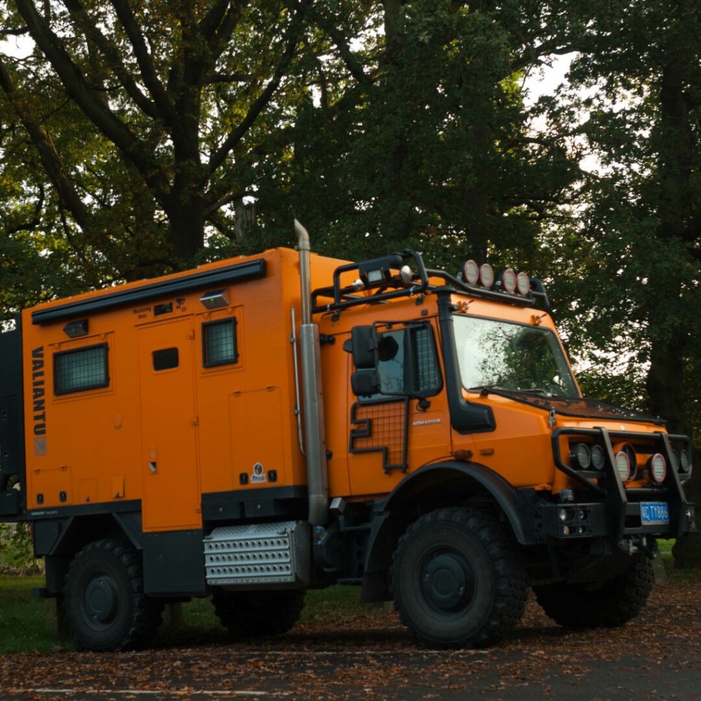 Photo of a large blocky orange vehicle in front of some trees