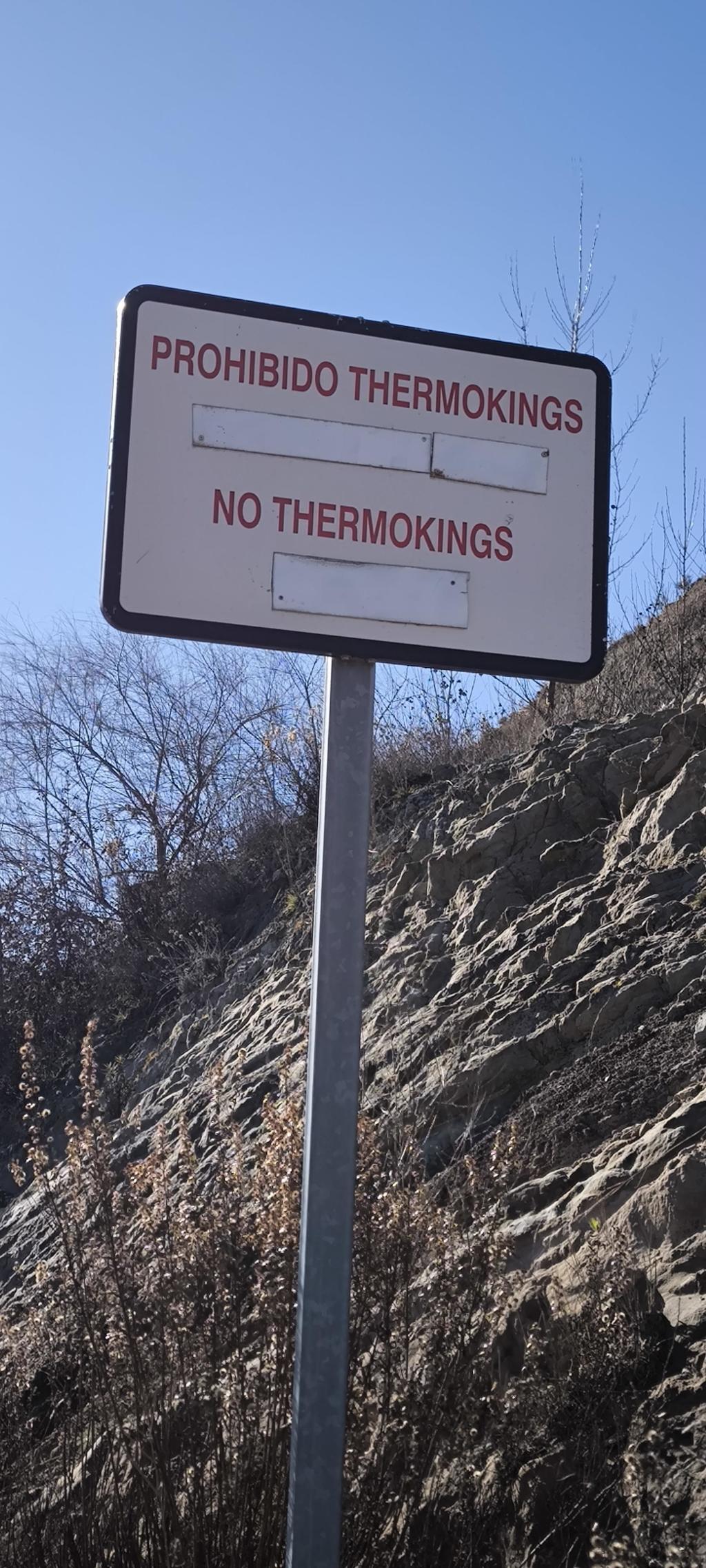 Un cartel pone PROHIBIDO THERMOKINGS
Y debajo: 
NO THERMOKINGS.
Se ve un talud, unos arbustos sin hojas. La señal del cartel tiene un mástil metálico. Hace sol. 
Esto es Medinaceli, por cierto