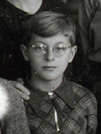 Black and white portrait of a young boy wearing a plaid jacket and round glasses.