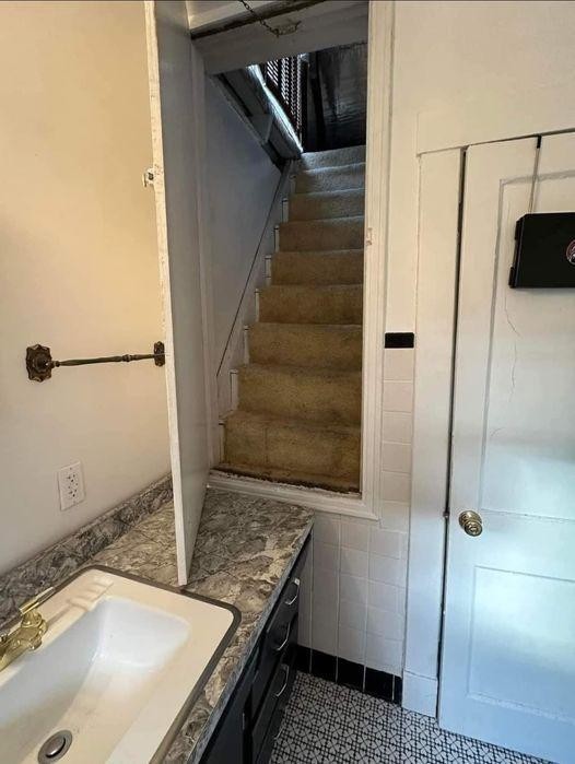 A very strange photo that someone took from a bathroom that has a door at the level of the countertop by the sink. In the photo, the door is open and there are super narrow stairs behind it leading upward to another room.