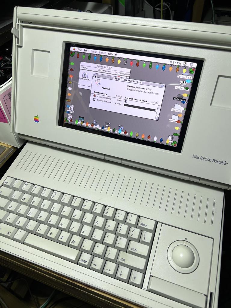 A Macintosh Portable luggable opened with System 7.5.5 and holiday lights around the desktop on color. 