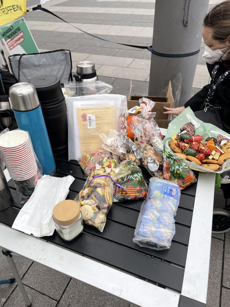 Ein Tisch mit Thermoskannen, Tassen, Zucker, verpackten Keksen, einem Tablett mit verschiedenen Gebäcken und einer Person, die Gegenstände arrangiert