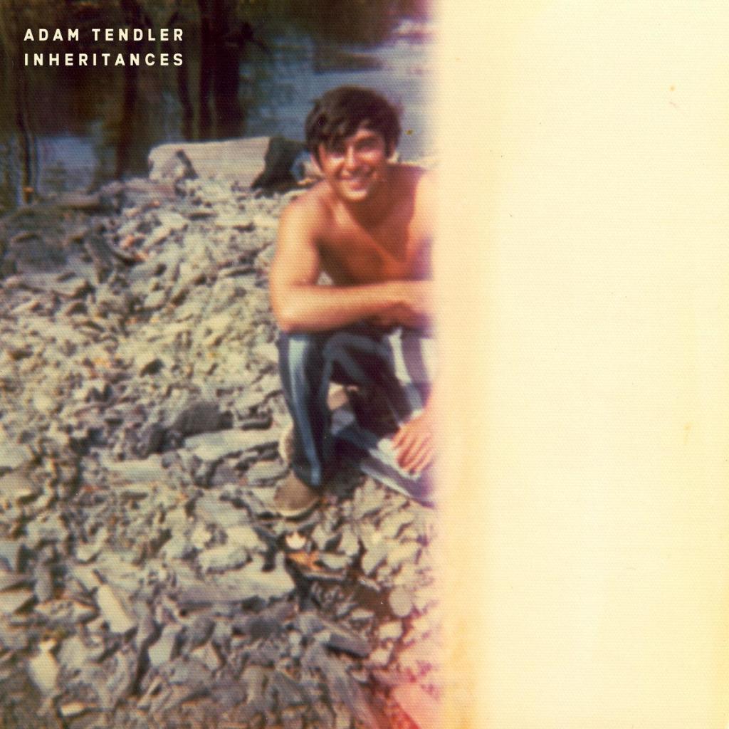 Cover of Adam Tendler’s New Amsterdam Records album “Inheritances”, featuring a split image with a photo of a young smiling, shirtless man on a rocky beach on the left, fading to yellow on the right.