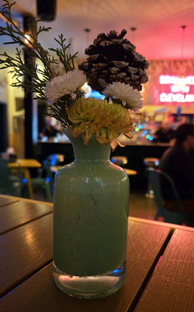 Small green bar with narrow opening.  In the base are a fellow flower and 2 white flowers plus some greenery