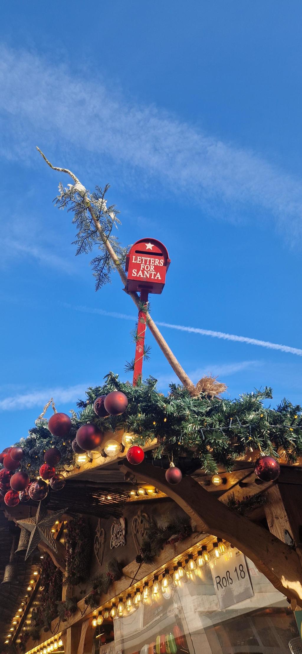 Ein roter Briefkasten auf dem Dach einer Weihnachtsbude. Darauf steht: Letter for Santa