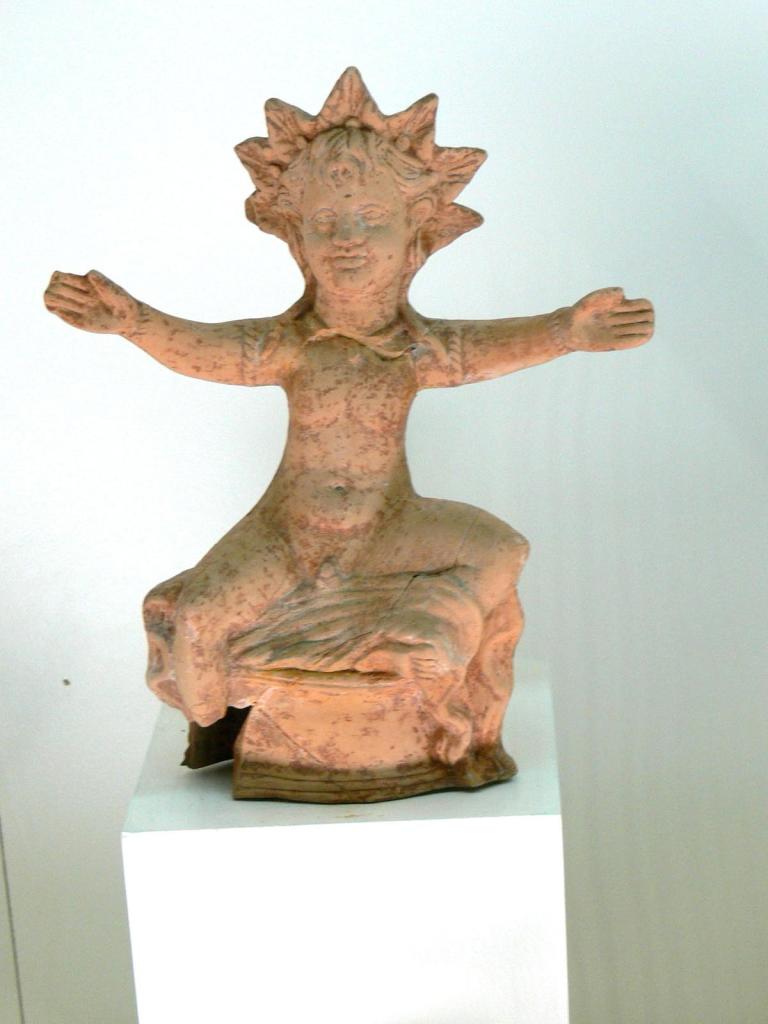 Terracotta figurine of Helios in the nude. The god is seated, his arms outstretched. The iconic seven-spiked sunray crown identifies him as the sun god.