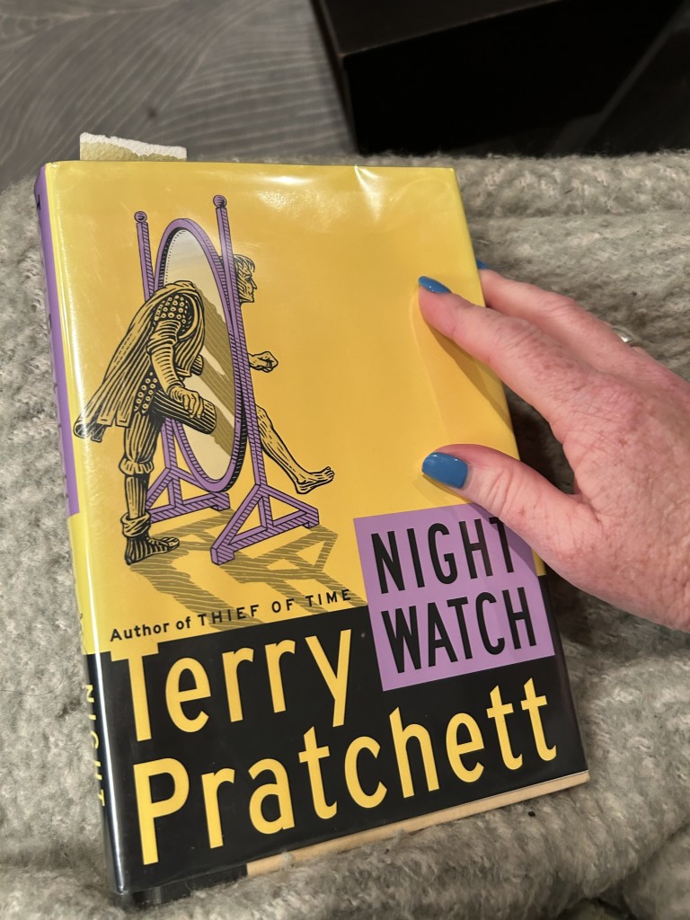 Photo of the cover of the book Night Watch by Terry Pratchett featuring a drawing of a man stepping through a mirror back in time