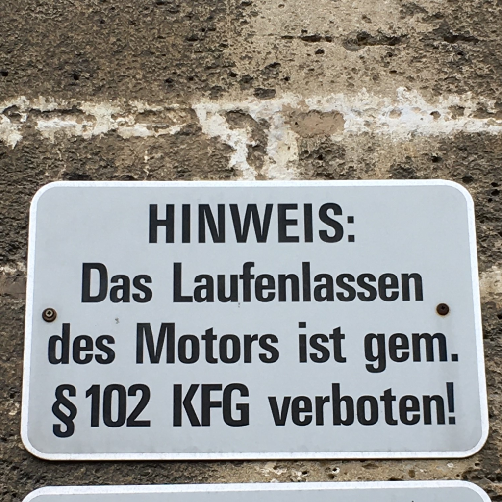 Foto von einem Schild mit Aufschrift: Das Laufenlassen des Motors ist gemäß §102 KFG  verboten