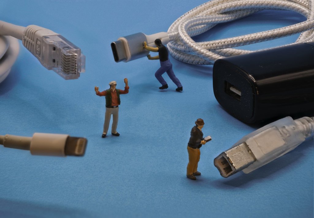 A collection of cables is surrounded by small figurines depicting people interacting with the cables. There is a USB A power plug, but all 4 cables have different connectors.