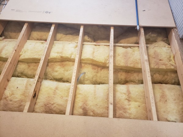 A view of the under-floor joists of a mobile home

The spacing is roughly 16"on center, and there is fiberglass insulation under the boards

Just above the middle of the picture, running left to right are a pair of quarter inch CPVC pipes to feed a bathroom

At top and bottom of the image are sheets of particle board, though the one above has some damage from mishandling, which can be seen right next to the broom handle extending down from the upper right