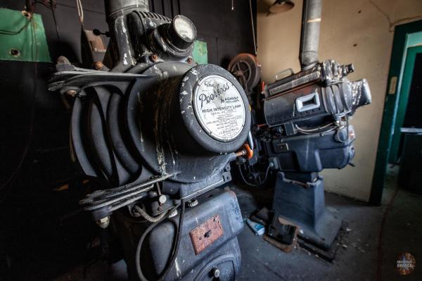 Closeup of the rear of a projector, with another in the background. A circular plate on the back reads "The Peerless Magnarc High Intensity Lamp"