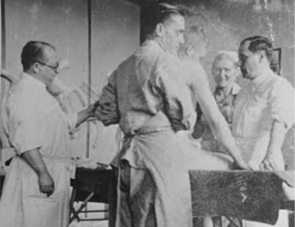 Several people in medical uniforms - three men and one woman, are standing around a table. 