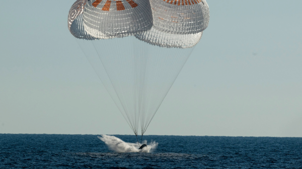 a cone-shaped spacecraft splashes down into open sea under three parachutes