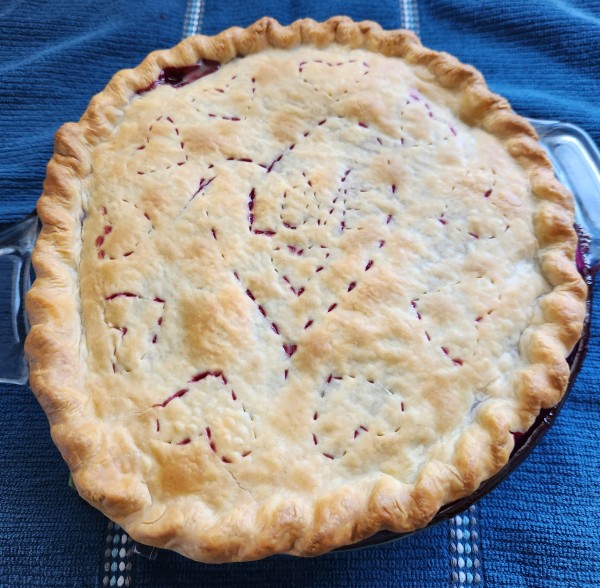 Raspberry and blackberry pie with heart-shaped vent design. The pie is cooling on a blue kitchen towel.