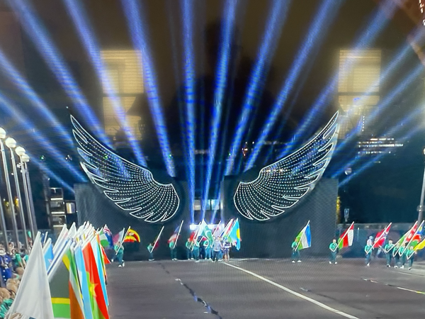 The flags of nations participating flank the bridge before the illuminated wings of doves of peace