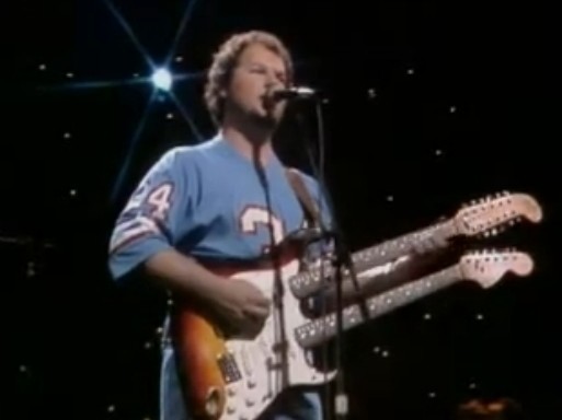 Christopher Cross in concert wearing an Earl Campbell jersey and playing a double-neck 3-tone burst Fender electric guitar.