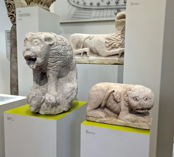 Ancient eroded marble sculptures of two lions. One is upright and appears to be screaming in horror. The other is in the fetal position and looks like a worrier. 