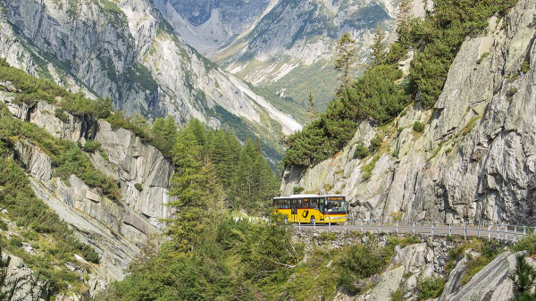 Ein gelber Postbus fährt auf einer Passstraße an einer Schlucht entlang.