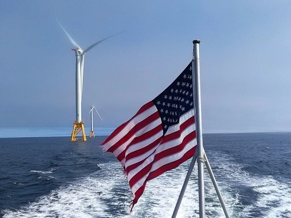 Looking aft from a vessel flying a large U.S. flag, toward two offshore wind turbines. I took this photo off Block Island, site of the first U.S. offshore wind farm, in 2017.