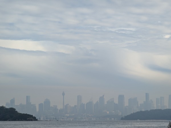 Under thick rain clouds a faint Sydney metropolitan skyline seen across Port Jackson 