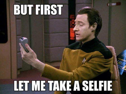 Lieutenant Commander Data from Star Trek the next generation holding a handheld device in hand and saying but first, let me take a selfie!