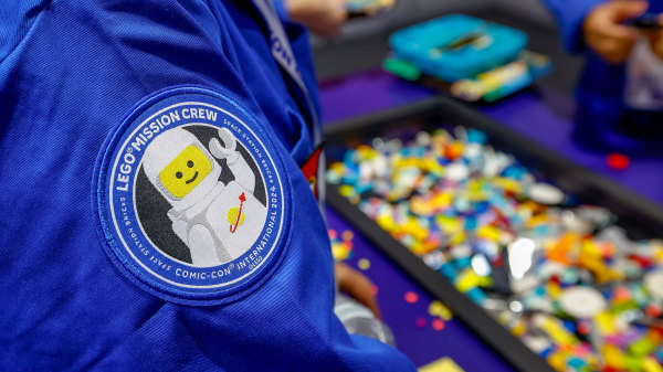 closeup of a patch on a blue shirt%2D which shows a spacesuited lego man smiling and waving. blurry bins of legos are in the background