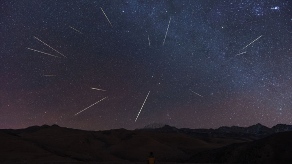 a dark mountainous landscape beneath a dark sky with many shooting stars