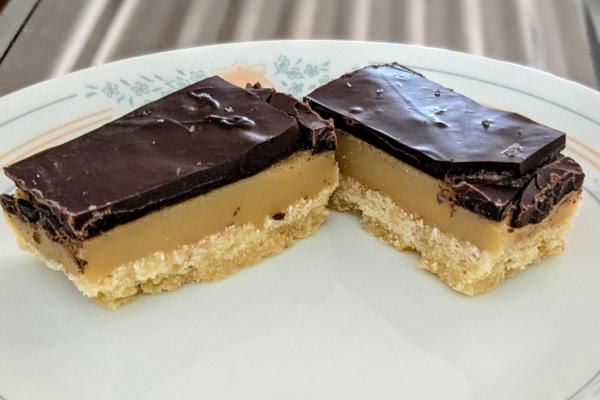 Two small slices of caramel slice AKA millionaire's shortbread on a white plate.