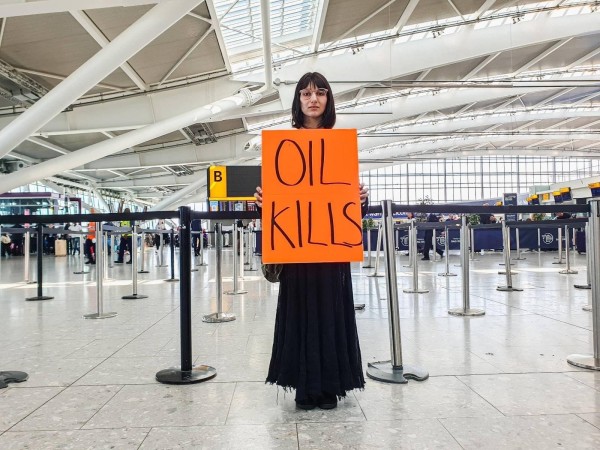 Mensch steht in einem Fliughafen mit einem Plakat auf dem steht "Oil kills"