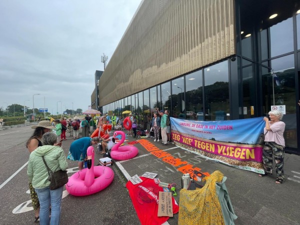 Viele bunte Menschen mit vielen bunten Bannern vor einem Flughafen