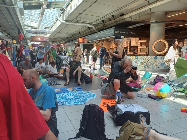 Viele bunte Menschen mit vielen bunten Bannern sitzen in einem Flughafen