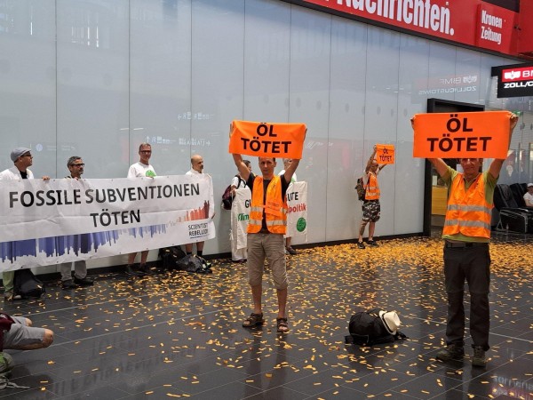 Banner "Fossile Subventionen töten". Menschen in orangen Westen halten orange Schilder "Öl tötet"