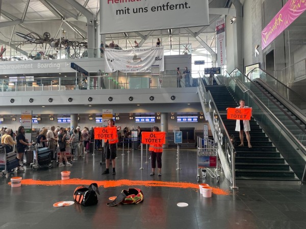 Menschen halten Schilder "Öl tötet", vor ihnen ist eine breite orange Linie auf dem Boden