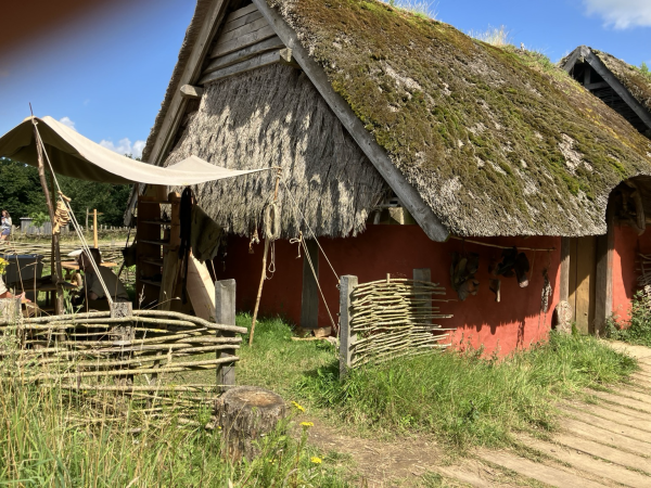 Reetgedecktes Wikingerhaus, rot bemalt mit Weidenzäunen umgrenzt