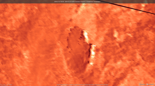 Glowing wall of flame, seen on infrared sensor, on the east of a wildfire scar